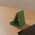 Angled Phone Stand in Matte Sage Green PLA, on a wooden desk