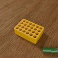 Battery Organizer (24x AAA) in Bright Yellow PLA, next to batteries on a wooden workbench