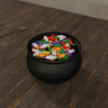 Cauldron Candy Dish in Matte Black PLA, filled with wrapped candy on a dark wooden table