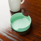 Coaster Caddy in Matte Mint PLA, next to a coffee mug on a wooden table