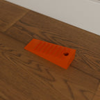 Grippy Door Stop Wedge in Bright Orange PETG, on a wooden floor