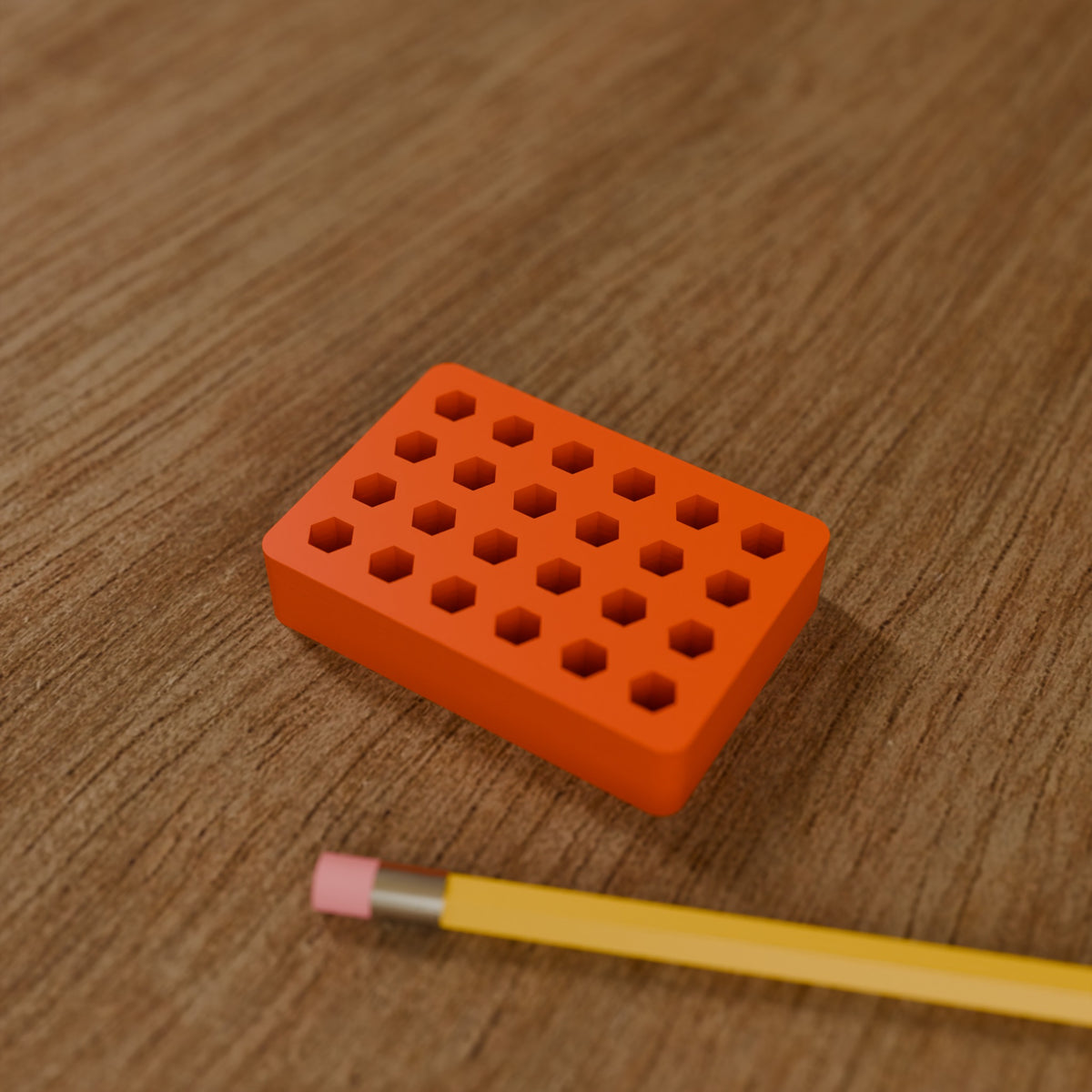 Hex Bit Organizer Block (24 bits) in Bright Orange PLA, next to a pencil on a wooden workbench