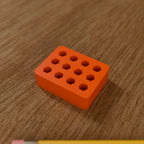 Hex Bit Organizer Block (12 bits) in Bright Orange PLA, next to a pencil on a wooden workbench