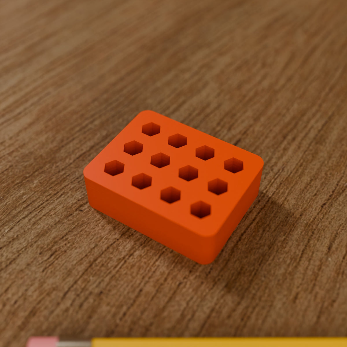 Hex Bit Organizer Block (12 bits) in Bright Orange PLA, next to a pencil on a wooden workbench