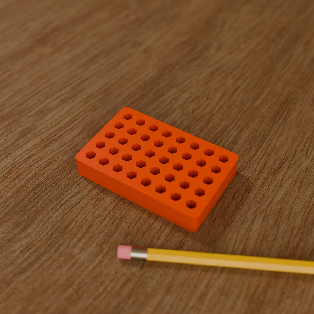 Hex Bit Organizer Block (40 bits) in Bright Orange PLA, next to a pencil on a wooden workbench