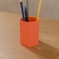 Hex Pen Cup (Standard 100 mm) in Matte Coral PLA, holding pencils on a wooden desk
