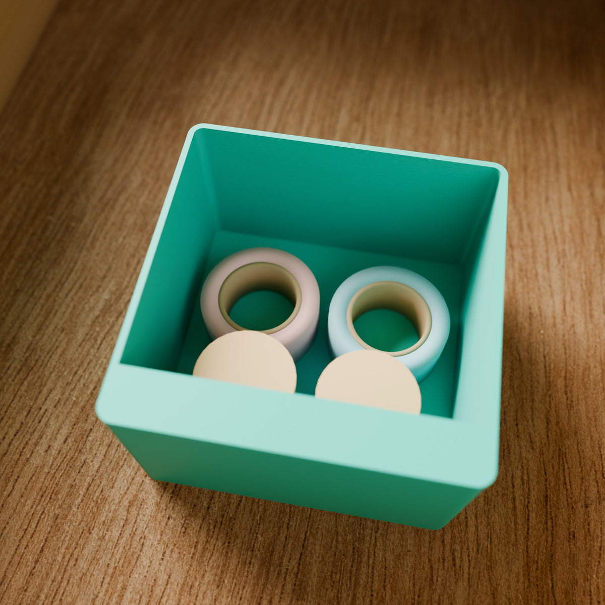 Modular Storage Bin (2x2) in Matte Teal PLA, holding tape rolls on a wooden surface