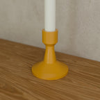 Taper Candle Holder in Matte Mustard PETG, holding a taper candle on a wooden shelf